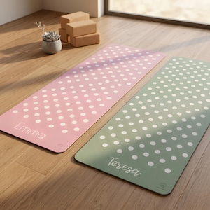May include: Two yoga mats, one pink and one green, are shown on a wooden floor. Both mats have a white polka dot pattern. The pink mat is labelled "Emma", and the green mat is labelled "Teresa".