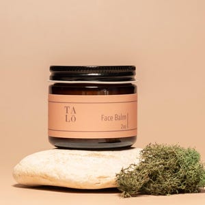 May include: A brown glass jar with a black lid containing a face balm. The jar has a label with the text "TALO" and "Face Balm 2oz".