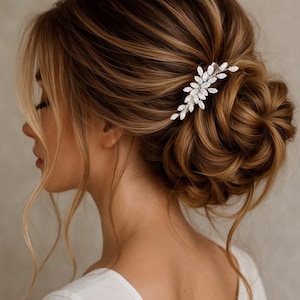 May include: A silver hair comb with a floral design, adorned with sparkling crystals, is placed in a woman's updo. The hair is a mix of light and dark brown tones, styled in loose waves and curls. The comb adds a touch of elegance to the hairstyle.