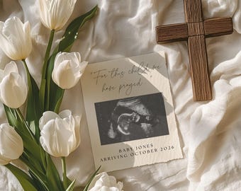 May include: A wooden cross and a card with an ultrasound image and the text "For this child we have prayed..." and "Baby Jones Arriving October 2026" are displayed with white tulips on a cream-colored fabric.
