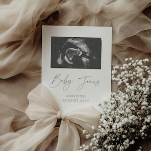 May include: A white card with a black and white ultrasound image of a baby. The card says "Baby Jones" in cursive and "Arriving August 2025".