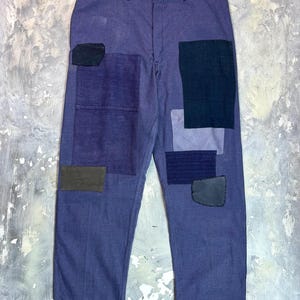 Puede incluir: Pantalones vaqueros azules con diseño de patchwork. Varios parches en diferentes tonos de azul y negro están cosidos. Los parches tienen diferentes formas y texturas. Los pantalones tienen un diseño clásico de cinco bolsillos.