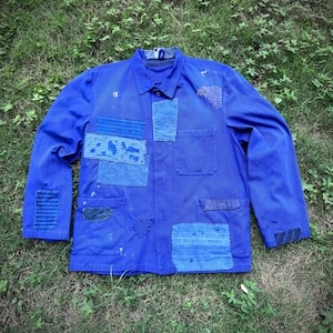 Peut inclure: Veste de travail bleu vif avec plusieurs patchs de différentes nuances de bleu. La veste, avec deux poches de poitrine, est posée sur de l'herbe verte. Des patchs sont cousus sur le devant et les manches.