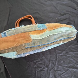 Pu&ograve; includere: Una borsa tote patchwork realizzata in denim e tessuto marrone. La borsa presenta un manico in pelle marrone e cuciture a vista. Il design incorpora varie tonalit&agrave; di denim blu e marrone, creando un aspetto unico e strutturato.