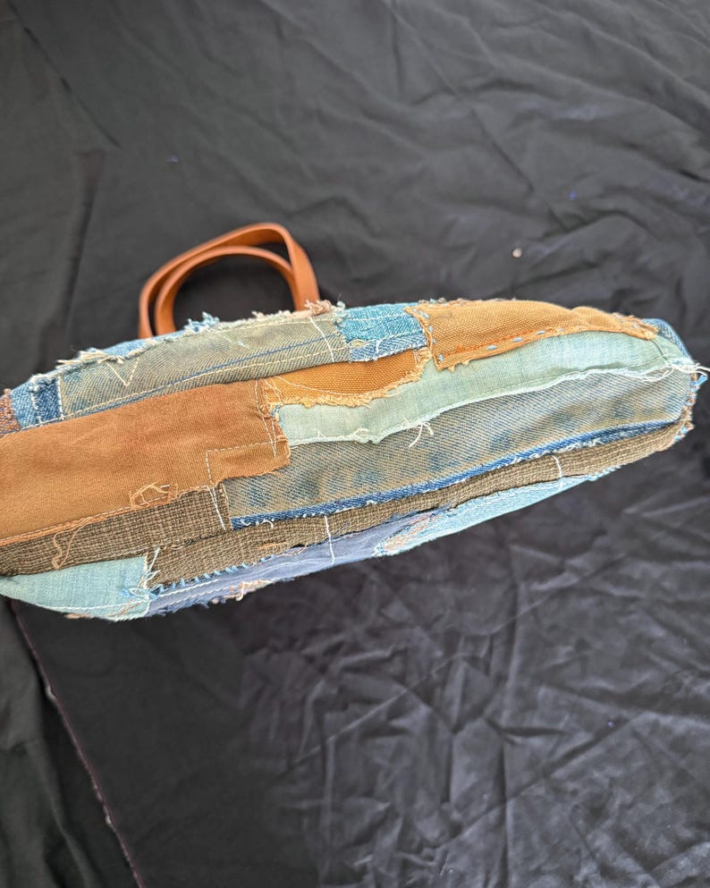 Pu&ograve; includere: Una borsa tote patchwork realizzata in denim e tessuto marrone. La borsa presenta un manico in pelle marrone e cuciture a vista. Il design incorpora varie tonalit&agrave; di denim blu e marrone, creando un aspetto unico e strutturato.