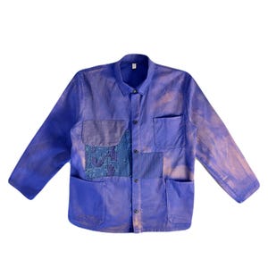 Puede incluir: Chaqueta de trabajo azul con cierre de botones, dos bolsillos en el pecho y dos bolsillos inferiores. La chaqueta presenta parches de diferentes tejidos azules y un aspecto descolorido y desgastado.
