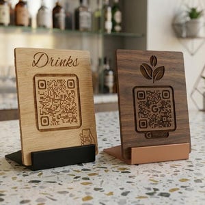Könnte beinhalten: Zwei hölzerne QR-Code-Schilder auf einer gesprenkelten Theke. Eines ist helles Holz mit "Drinks" und einem QR-Code. Das andere ist dunkles Holz mit einem Kaffeebohnen-Design und einem QR-Code. Beide haben einen Ständer.
