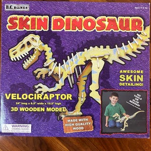 May include: A purple box featuring a 3D wooden model of a Velociraptor dinosaur. The model is 61 cm long, 22 cm wide, and 39 cm high. The box also includes the text "Skin Dinosaur" and "Awesome Skin Detailing!"