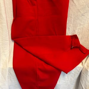 Op de afbeelding: Een rode broek met een knoop- en ritssluiting. De broek heeft een rechte pijp en is gemaakt van een gladde stof.