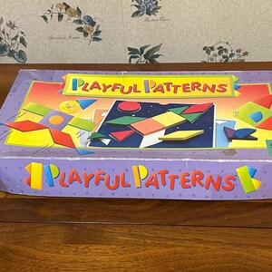 May include: A rectangular box for the game "Playful Patterns" with a purple lid and colourful geometric shapes. The box features the game's title in yellow and orange, with a background of a sunset and stars.