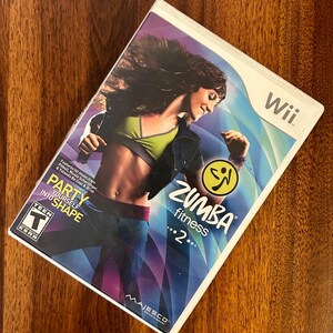May include: A Wii game case for Zumba Fitness 2. The cover features a woman in workout attire dancing. The game's title and logo are prominently displayed. The case also includes the text "Party Yourself Into Shape."