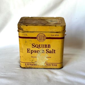 May include: A yellow metal tin with red and black lettering. The tin contains Squibb Epsom Salt, 1 lb. The tin is labeled "Recryst. Imp. panel purity" and "E-R-Squibb, Manufacturing Chemists to the Medical Profession since 1858, New York."