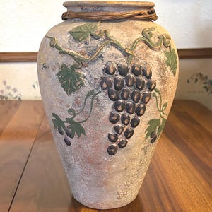 May include: A white ceramic mug with a black handle and the text "But First, Coffee" in a bold, black font. The mug is set against a blurred background, suggesting a cozy setting.