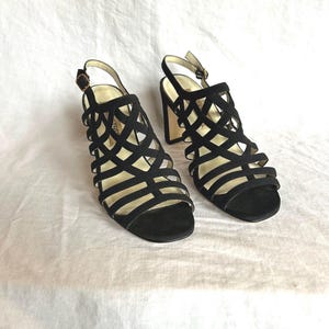 May include: Black suede heeled sandals with a caged design and an ankle strap.