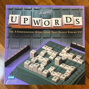 May include: A board game box for Upwords, a 3-dimensional word game from Parker Brothers. The box is purple with the game title in large white letters. The game board and letter tiles are visible, with the text "The 3-Dimensional Word Game That Really Stacks Up!"