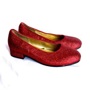 Op de afbeelding: Een paar rode glitter ballerina's met een lage hak. De schoenen hebben een spitse neus en zijn gemaakt van een glinsterende stof.