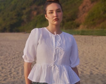 May include: A white linen blouse with a ruffled hem and a tie at the neckline. The blouse has a relaxed fit and is perfect for a casual summer look.