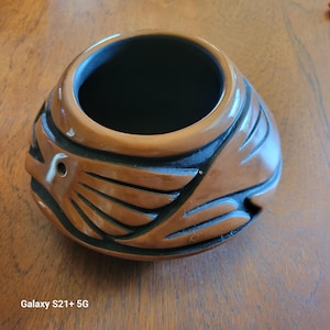 May include: A brown ceramic pot with black geometric designs. The pot has a round shape and a wide opening.
