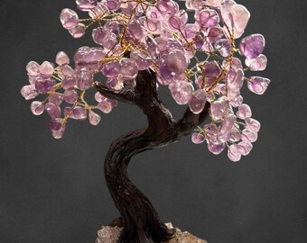 Könnte beinhalten: Ein lila Amethyst-Kristallbaum mit einem braunen Holzstamm und einer Basis. Der Baum besteht aus Draht und hat viele Äste mit Amethyst-Kristallen. Die Basis besteht aus einem natürlichen Stein mit einer rauen Textur.