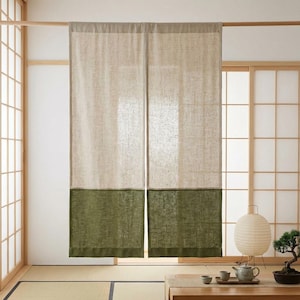 Op de afbeelding: Een beige en olijfgroen linnen gordijn hangt voor een traditionele Japanse schuifdeur. Het gordijn is verdeeld in twee secties, met een effen olijfgroene onderkant en een beige bovenkant. De kamer heeft een tatami-matvloer en een houten tafel.
