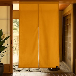 May include: A mustard-yellow curtain hangs in a doorway, with a split down the middle. The curtain is made of a textured fabric. A potted plant with white flowers sits to the left. The floor is made of dark wood.