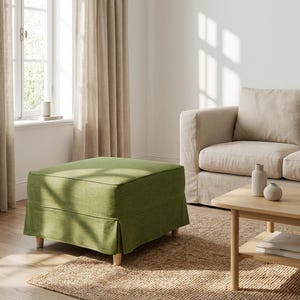 May include: A square, olive green ottoman with a skirted base and light wooden legs. The ottoman is in a living room setting, with a beige sofa, wooden coffee table, and natural fiber rug.