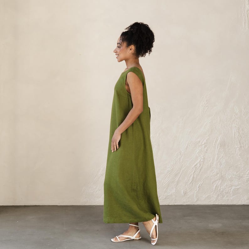 May include: A sleeveless, olive green maxi dress. The dress has a simple, flowing design and a scoop neckline. The model is wearing white sandals. The dress is made of a lightweight fabric, perfect for warm weather. The dress is a versatile piece that can be dressed up or down.