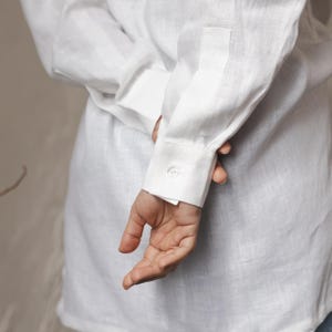 May include: A white linen shirt with a buttoned cuff. The shirt is folded and the cuff is visible.