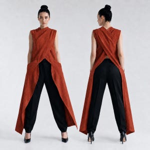 May include: A sleeveless, rust-colored tunic with a wrap-style front and a long, open-back design, paired with solid black trousers. The tunic features a high neckline and side pockets, while the trousers have a straight-leg cut and a clean finish.