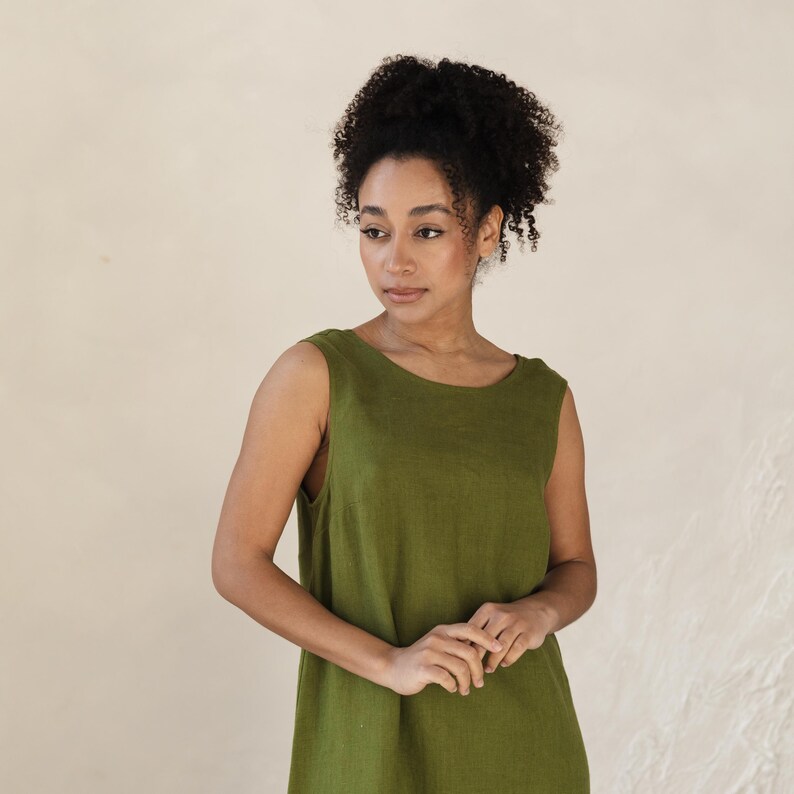 May include: A sleeveless, olive green dress with a scoop neckline. The dress is made of a soft, textured fabric and has a simple, elegant design. The model is wearing the dress and looking to the side.