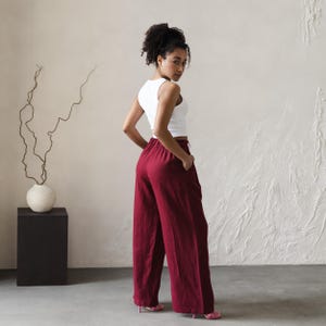 May include: A woman wearing a white tank top and wide-legged burgundy pants. The pants have a high waist and are made of a soft, flowing fabric.