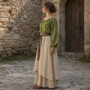 May include: A long-sleeved olive green blouse with a gathered neckline paired with a floor-length beige skirt featuring a layered hem and a brown fabric belt tied at the waist. The outfit consists of a solid-colored top and a neutral-toned skirt.