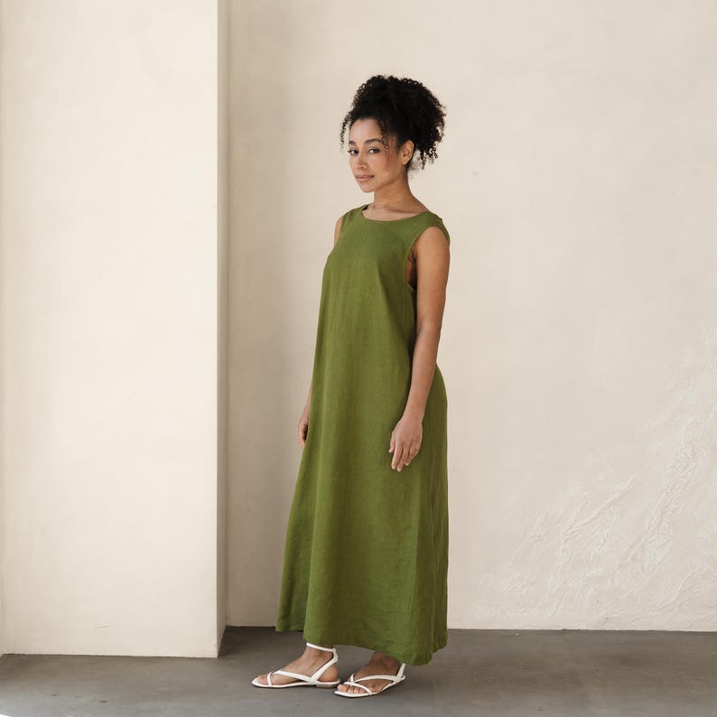 Sleeveless green linen maxi dress for women, styled in a minimalist neutral-toned room. This relaxed-fit summer dress features a round neckline and flowy silhouette, perfect for warm weather or layering year-round. Made from breathable natural fabric—ideal for cottagecore, boho, or slow fashion wardrobes.