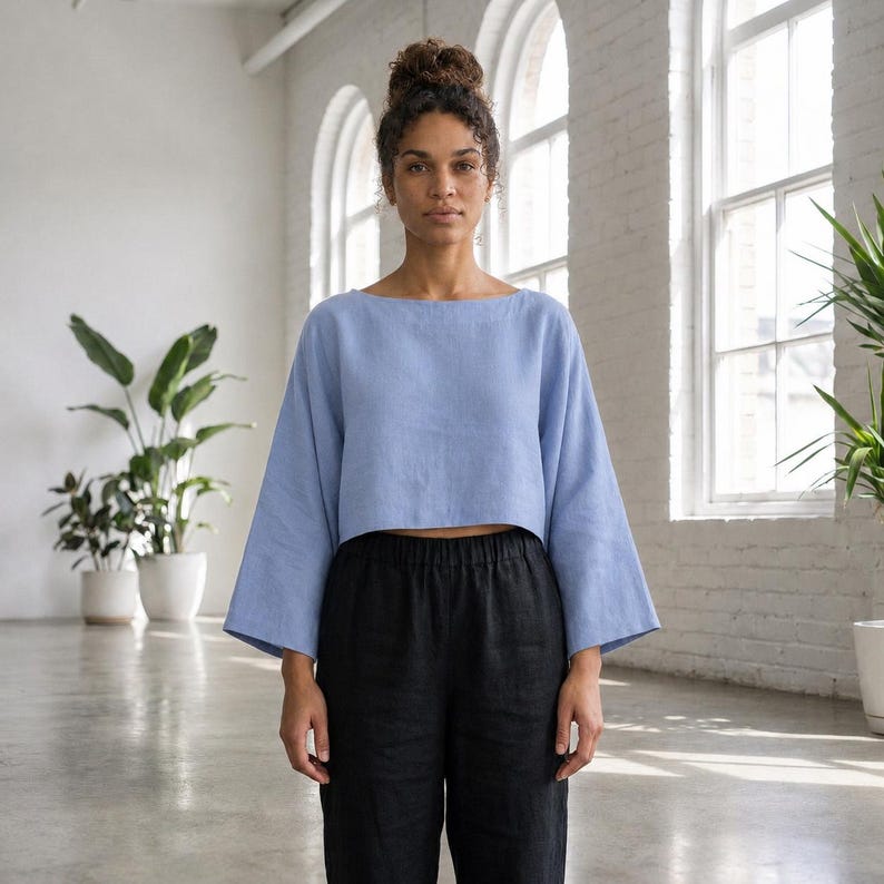 Puede incluir: Una blusa corta azul claro con mangas anchas y cuello barco, combinada con pantalones negros. La blusa est&aacute; hecha de una tela suave y fluida. El conjunto es sencillo y elegante, adecuado para ropa casual.