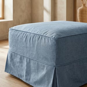 May include: A square, light blue ottoman with a tailored skirt. The ottoman is upholstered in a textured fabric and features a piped edge detail. The design is simple and modern, suitable for living rooms or bedrooms.