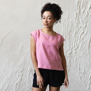 May include: A pink, cap-sleeved top and black shorts. The top has a round neckline and a loose fit. The shorts are high-waisted and have a relaxed fit. The outfit is simple and casual, suitable for warm weather.
