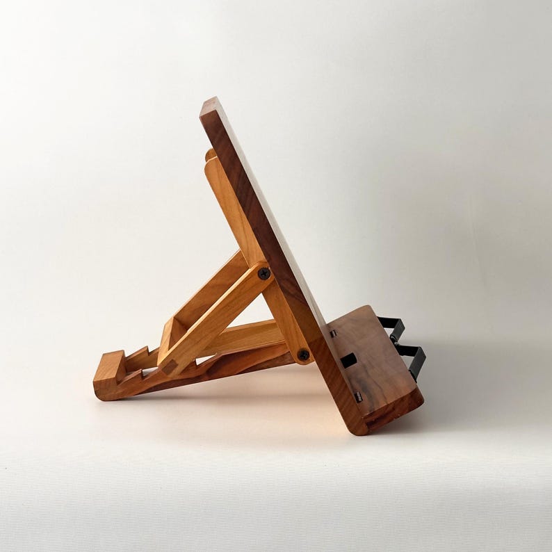 May include: A wooden book stand with a light brown and dark brown finish. The stand is adjustable and features a sloped surface to hold a book. The stand has a rectangular base and a black metal support.