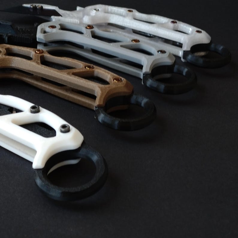 May include: A set of four knives with different colored handles. The handles are made of a textured plastic and have a ring on the end. The knives are arranged in a row, with the black handle knife at the bottom and the white handle knife at the top.