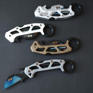 May include: Four different styles of pocket knives with black handles and various colored blades. The knives have a unique design with a ring on the handle.