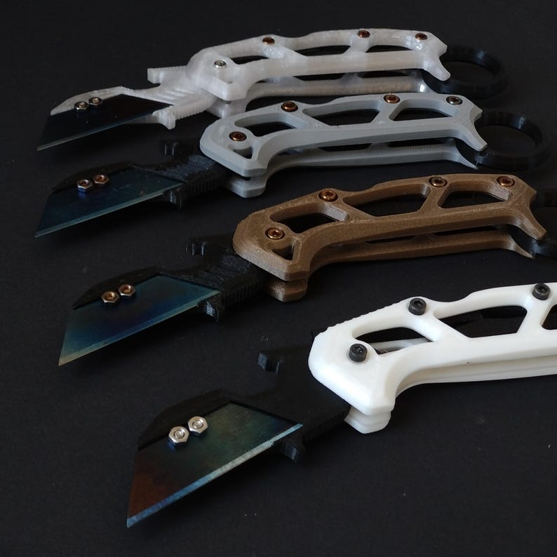 May include: Four utility knives with different colored handles. The handles are white, gray, brown, and white. The blades are all black and have a slight curve to them.