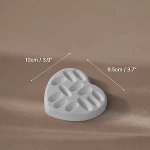 A white heart-shaped plaster ring dish used as a jewelry display prop for gold rings.