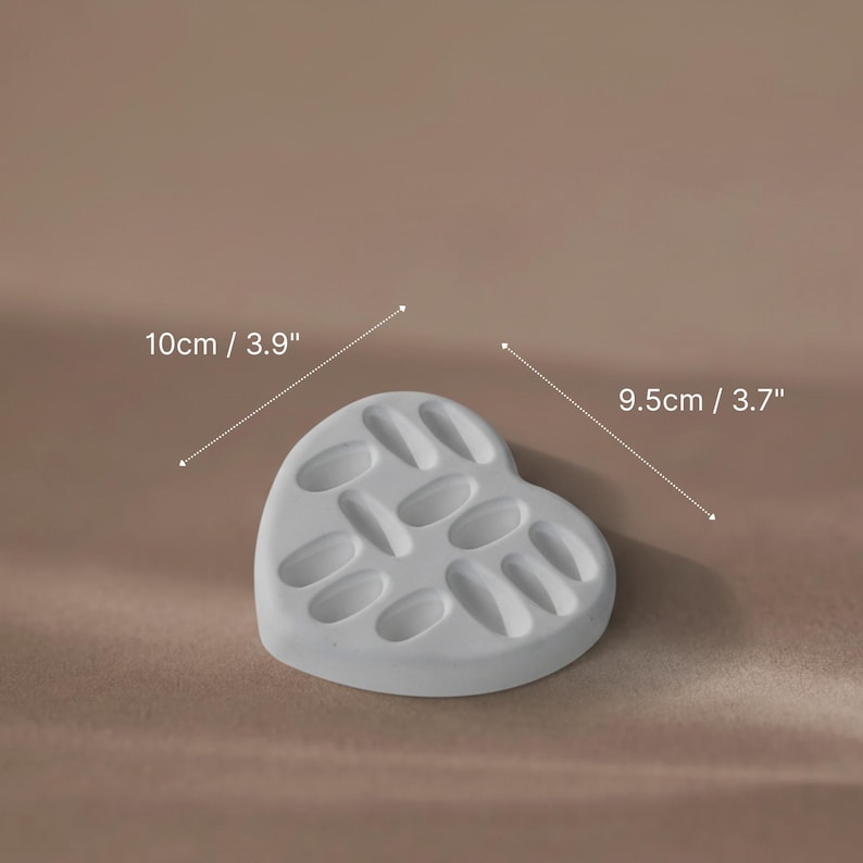 A white heart-shaped plaster ring dish used as a jewelry display prop for gold rings.
