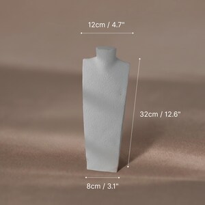 A white textured plaster necklace mannequin bust used as a jewelry display stand for a pearl necklace.