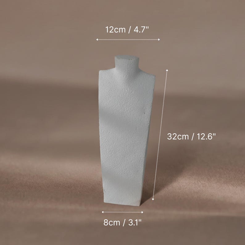 A white textured plaster necklace mannequin bust used as a jewelry display stand for a pearl necklace.