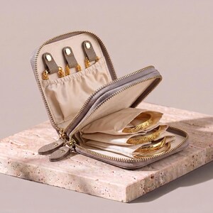Internal view of the leather jewelry pouch showing the cream-colored accordion-style inserts filled with gold bracelets.
