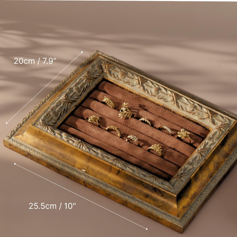 An ornate, antique gold picture frame repurposed as a jewelry display with a brown velvet ring holder inside.