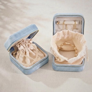 Può includere: Due portagioie aperti in velluto blu chiaro con cerniere dorate. Un astuccio contiene un sacchetto beige con coulisse, l'altro un braccialetto dorato con perle. Il secondo ha anche una sezione per collane.