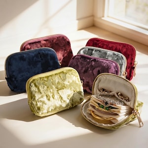 May include: A collection of velvet jewelry cases in various colors, including navy, burgundy, and olive green. One case is open, revealing jewelry. Each case has a gold zipper closure.