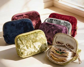May include: A collection of velvet jewelry cases in various colors, including navy, burgundy, and olive green. One case is open, revealing jewelry. Each case has a gold zipper closure.