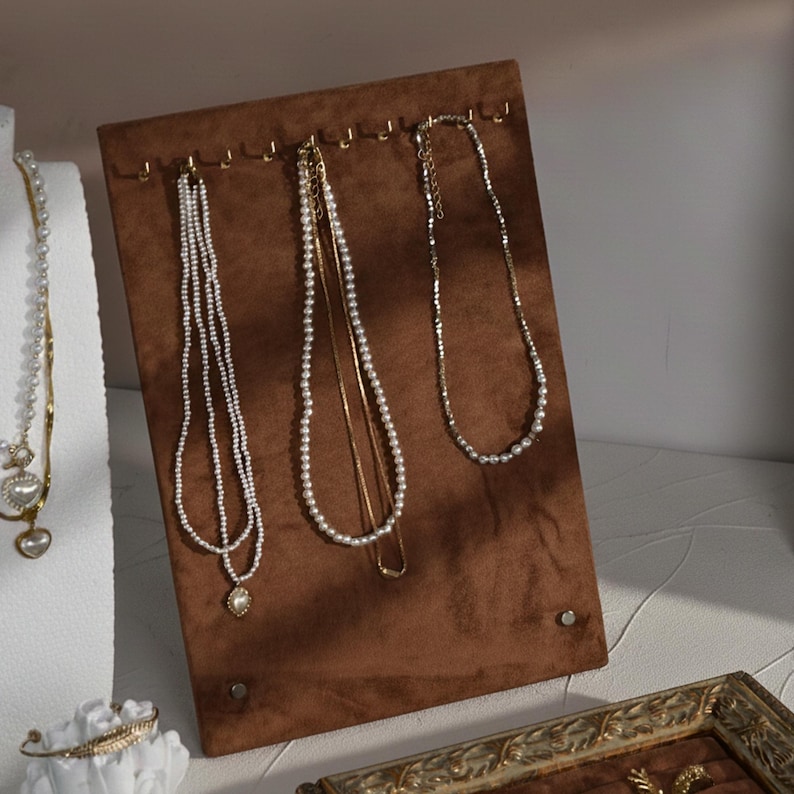 A vertical brown velvet jewelry display board with gold hooks for hanging pearl and gold necklaces.